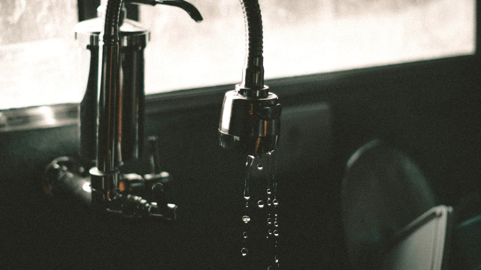 Water dripping from a kitchen faucet into the sink, illustrating a small controlled plumbing leak