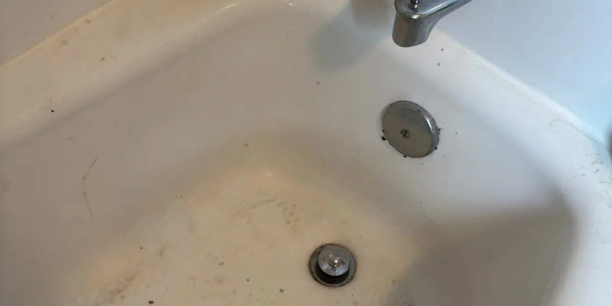 Tub spout, overflow plate and drain in a white bathtub with soil in the basin, on a Rockland drain call